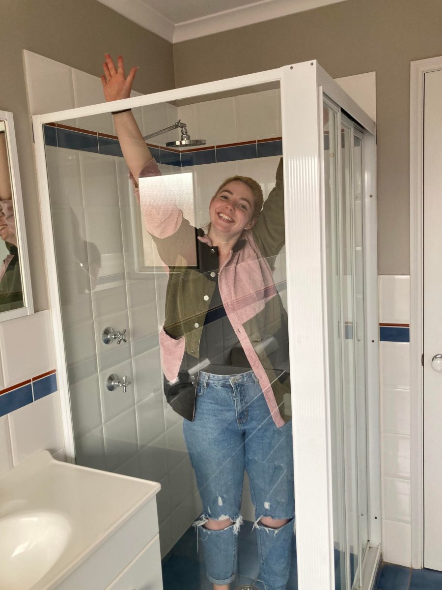 Laura Johnston holding her hands up in a transparent shower cubicle while fully clothed.
