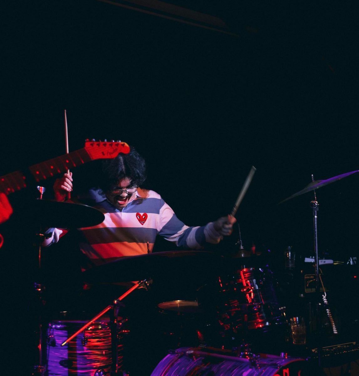 Aaron drumming at a gig with only one spotlight on him and the background black.