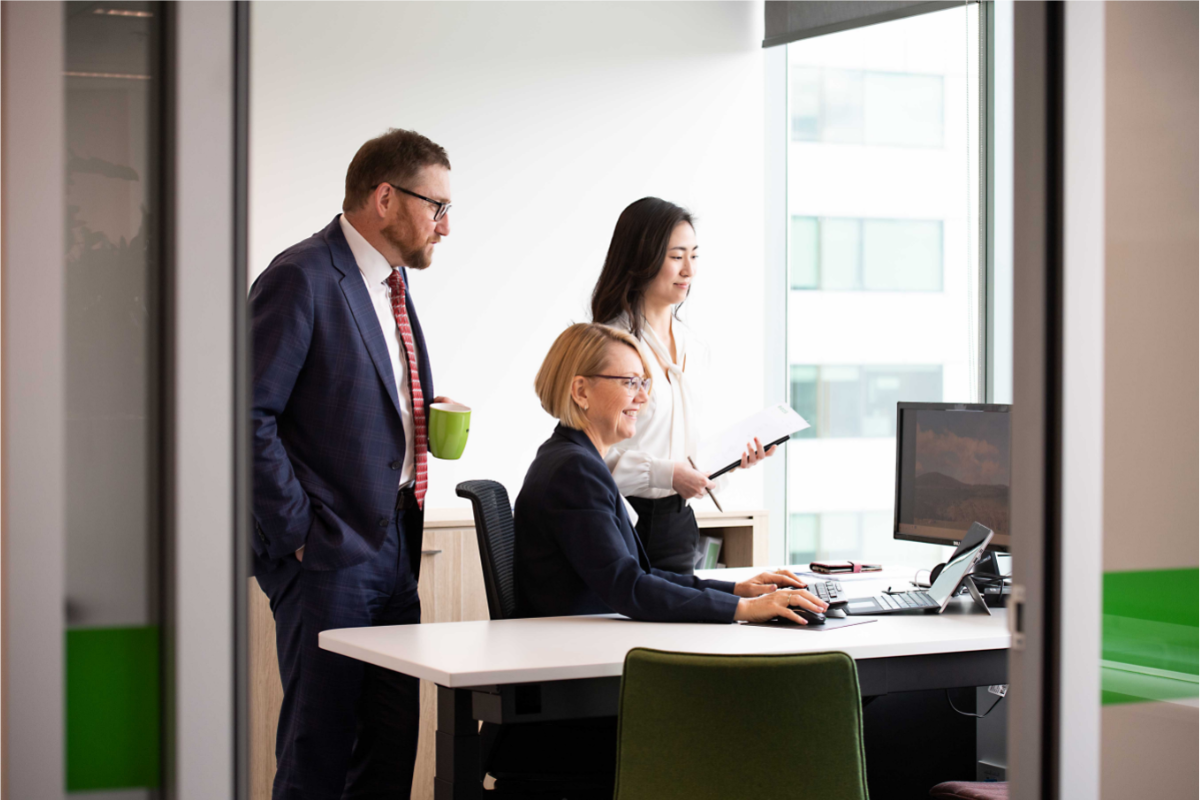 three people sitting at a desk looking at a computer screen