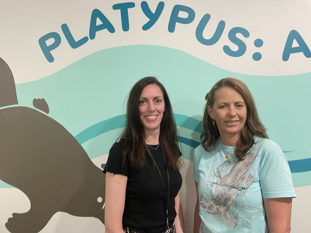 Two women in front of platypus sign