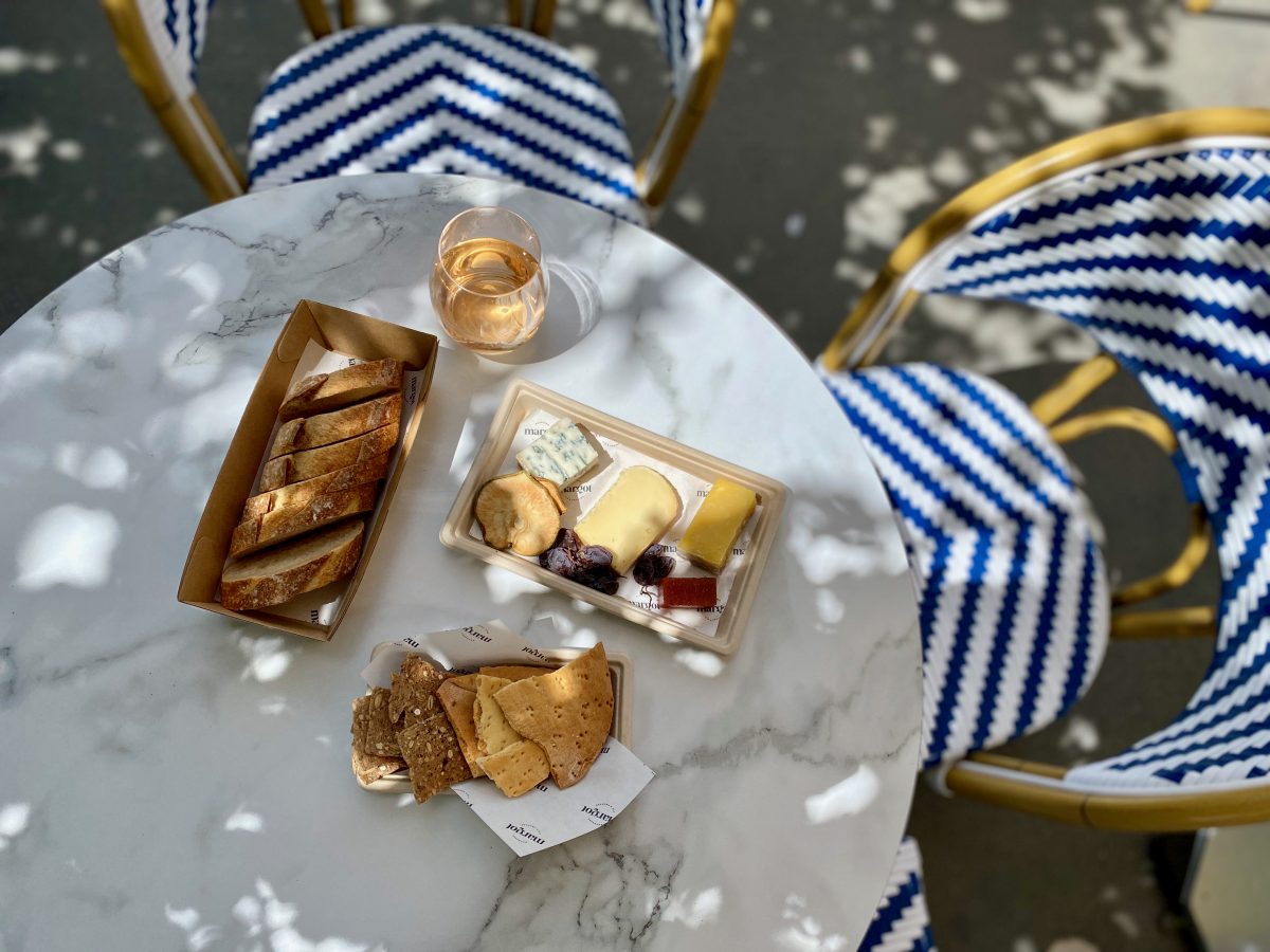 Cheese board under dappled sunlight with blue and white chairs Margot