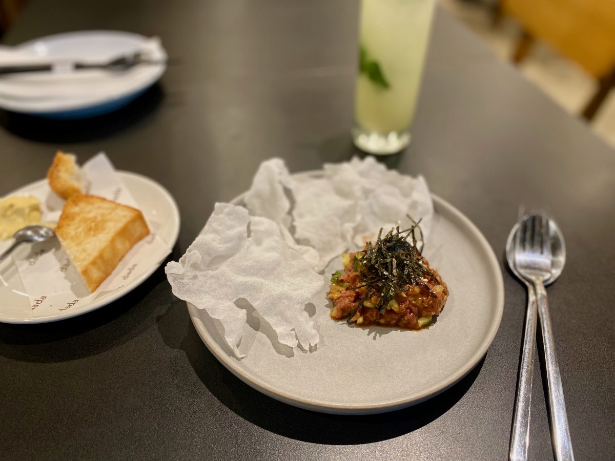 Beef tartare with white rice crisps on a black table at Dada.