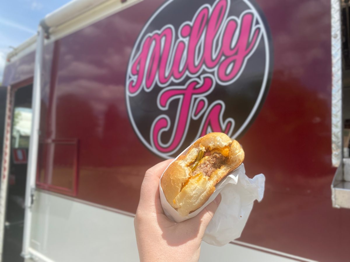 Burger with bite mark in front of Milly J's Logo.