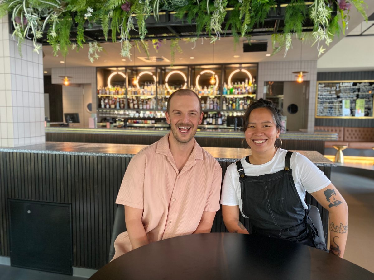 Nick Muir in pink shirt sits with Adrianne Davo in chef's apron in front of the bar at Luna