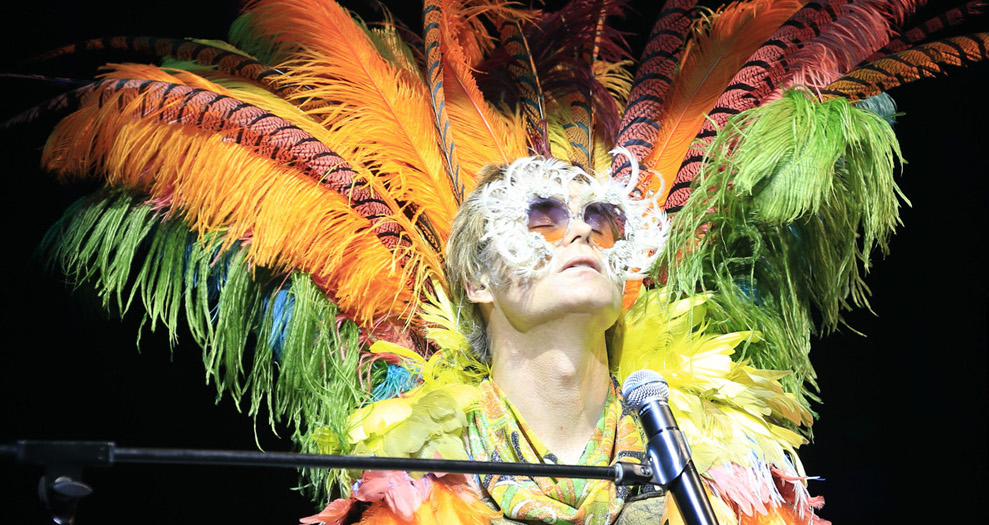 Man dressed is flamboyant feathers in front of a microphone