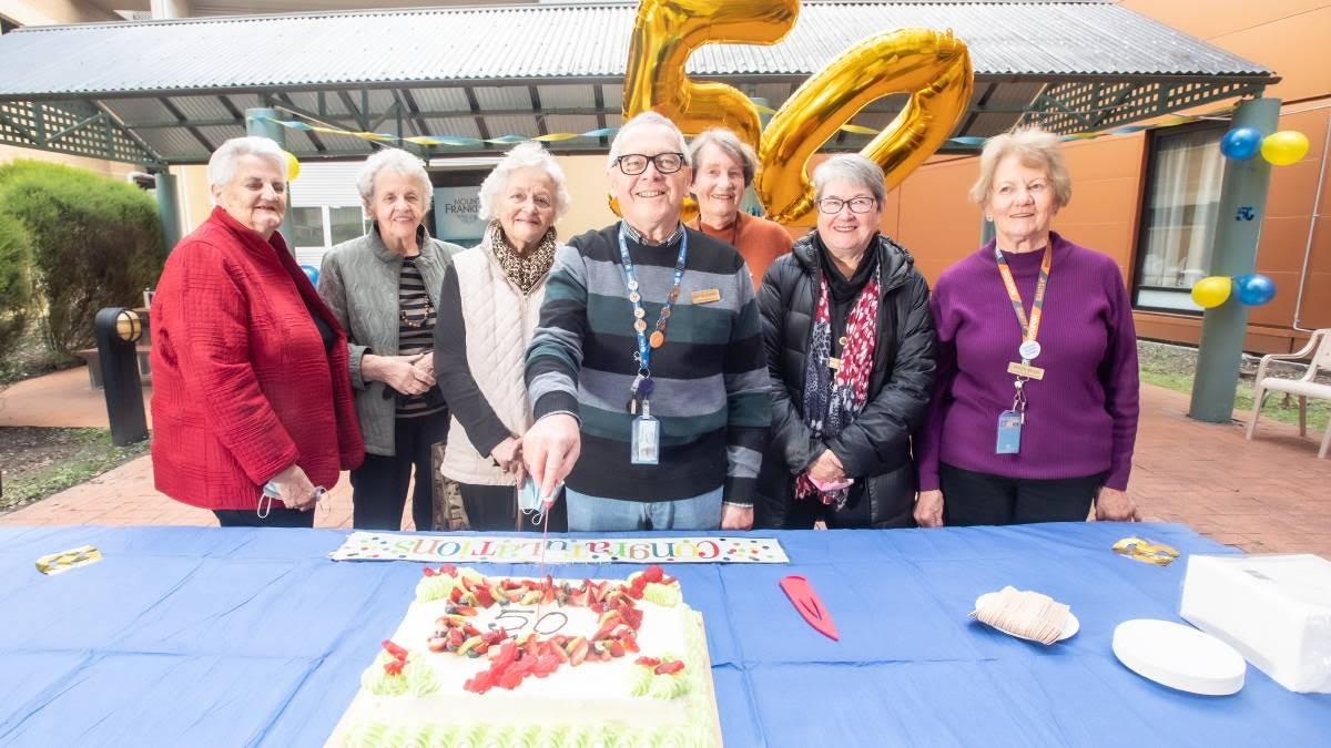 Seven Canberra Hospital Auxiliary Service volunteers slicing into the auxiliary service's 50th anniversary cake.