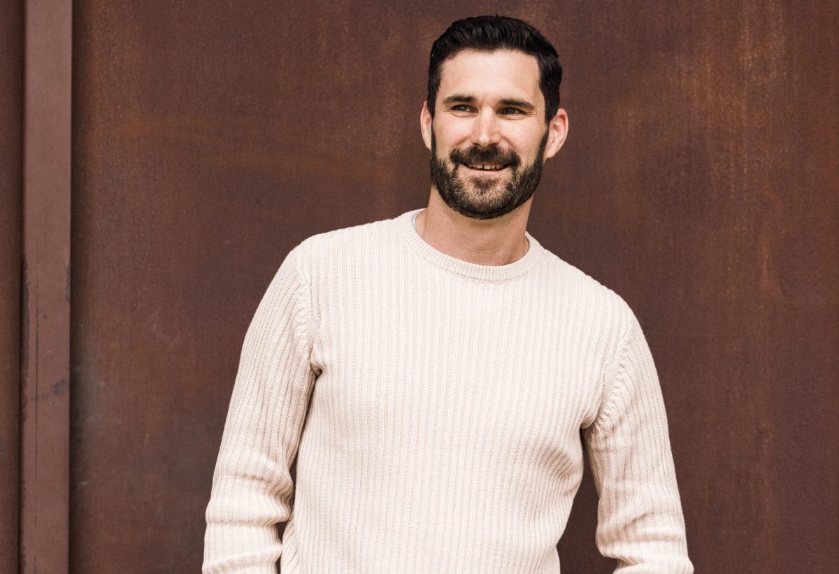 James Souter wears white jumper and smiles with hands in pockets