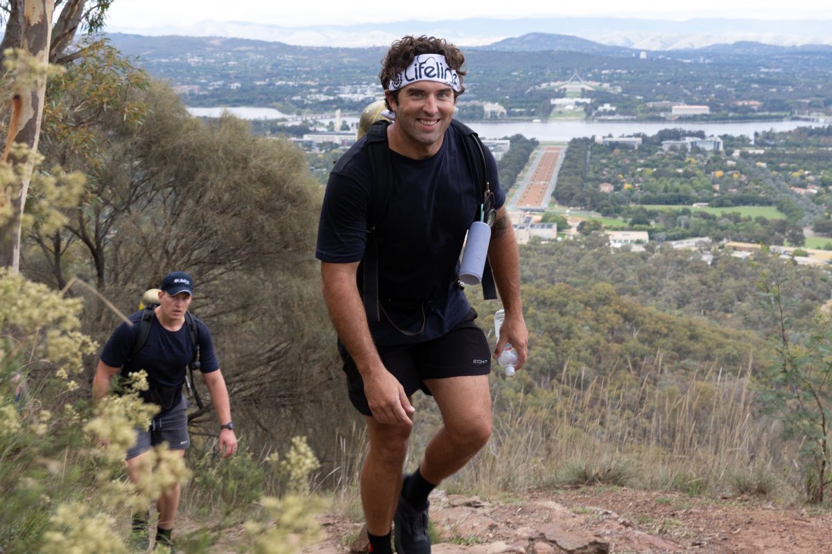 A man participating in the 2022 Ainslie to Everest climb in the foreground with Canberra's Parliament in the background