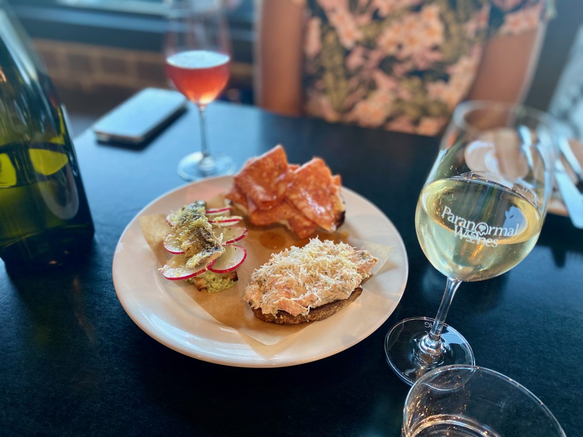 Three pieces of toast with different toppings on a plate with two glasses of wine