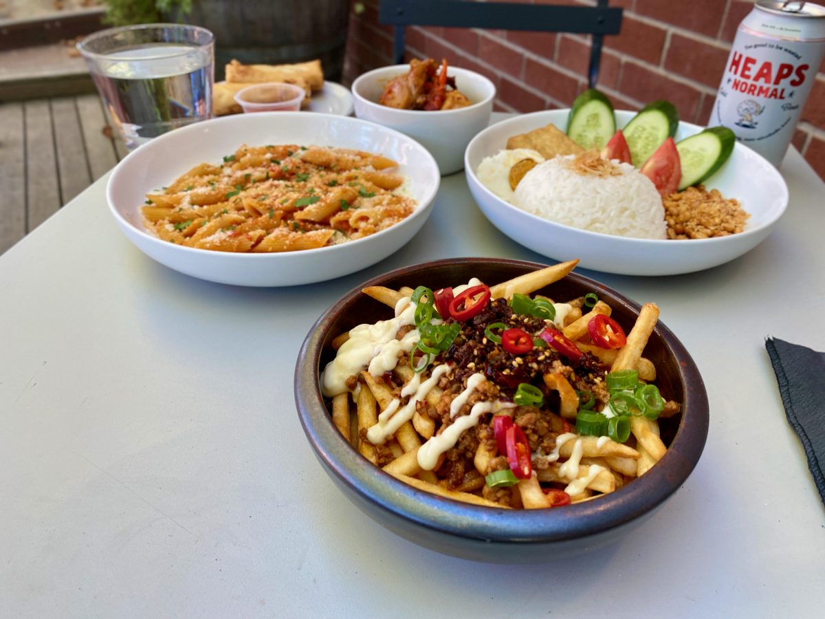 Bowl of loaded fries covered in chilli with pasta in the background