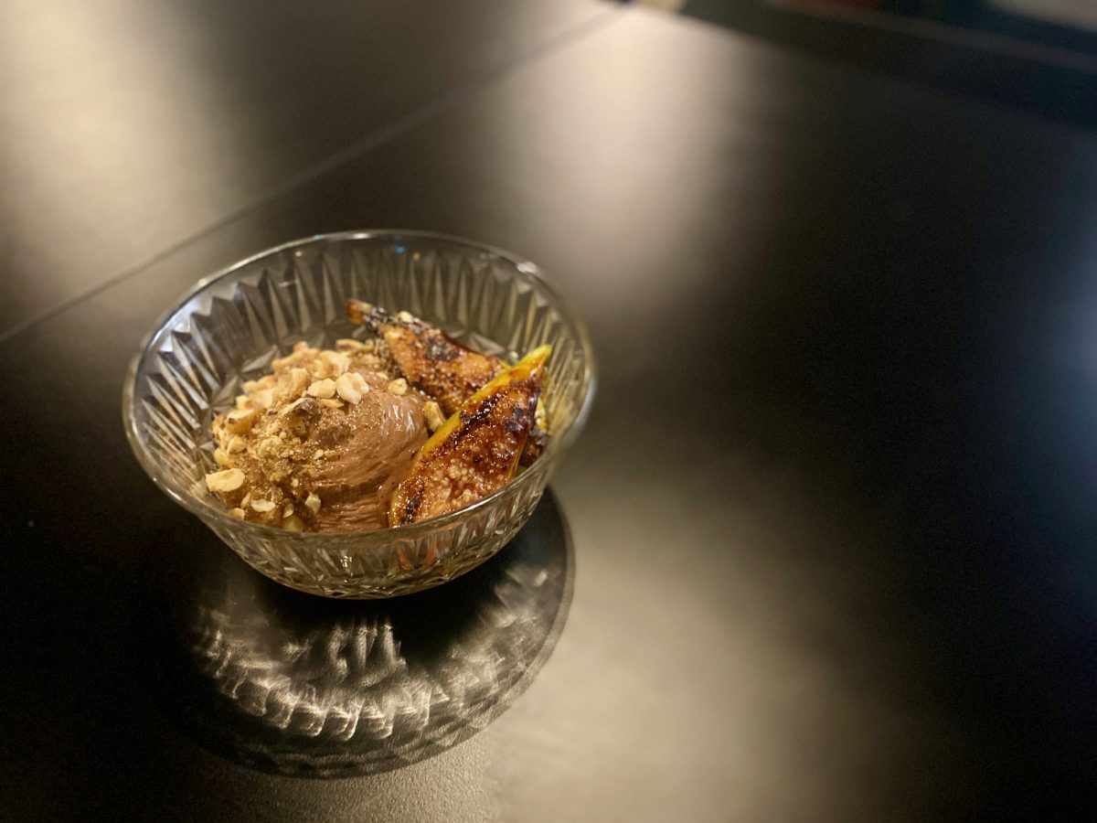 A glass bowl with chocolate mousse, nuts and grilled figs sits on black table