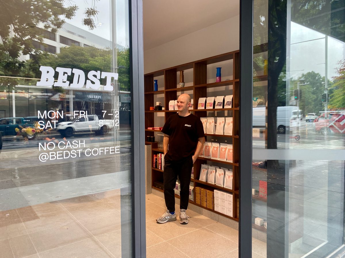 In the foreground Bedst logo with opening hours and James standing in front of the shelf of coffee