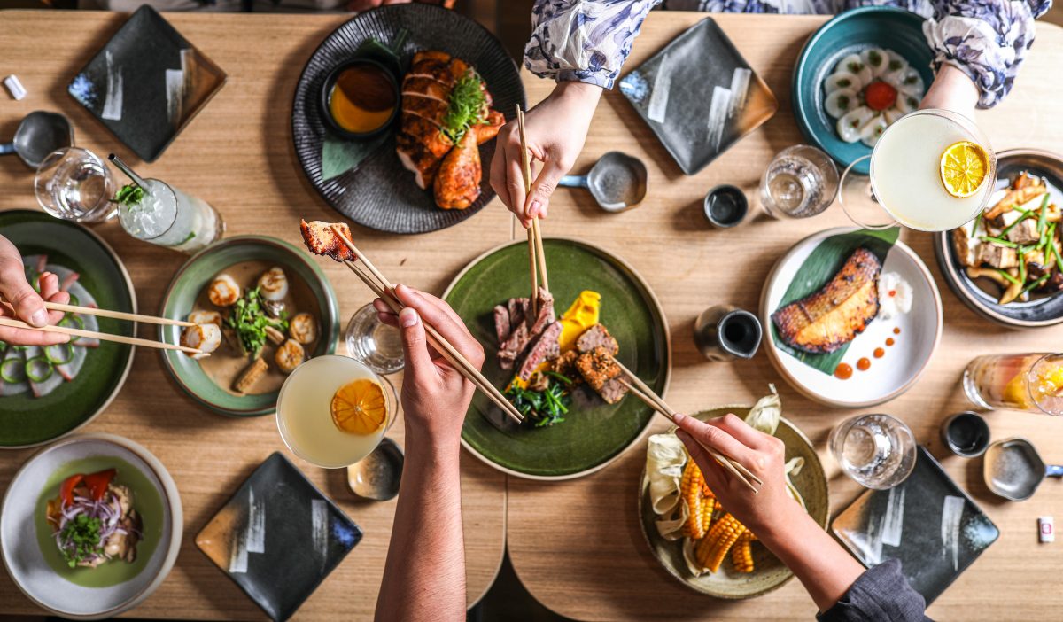 table covered in beautifully presented dishes with hands holding chopsticks 