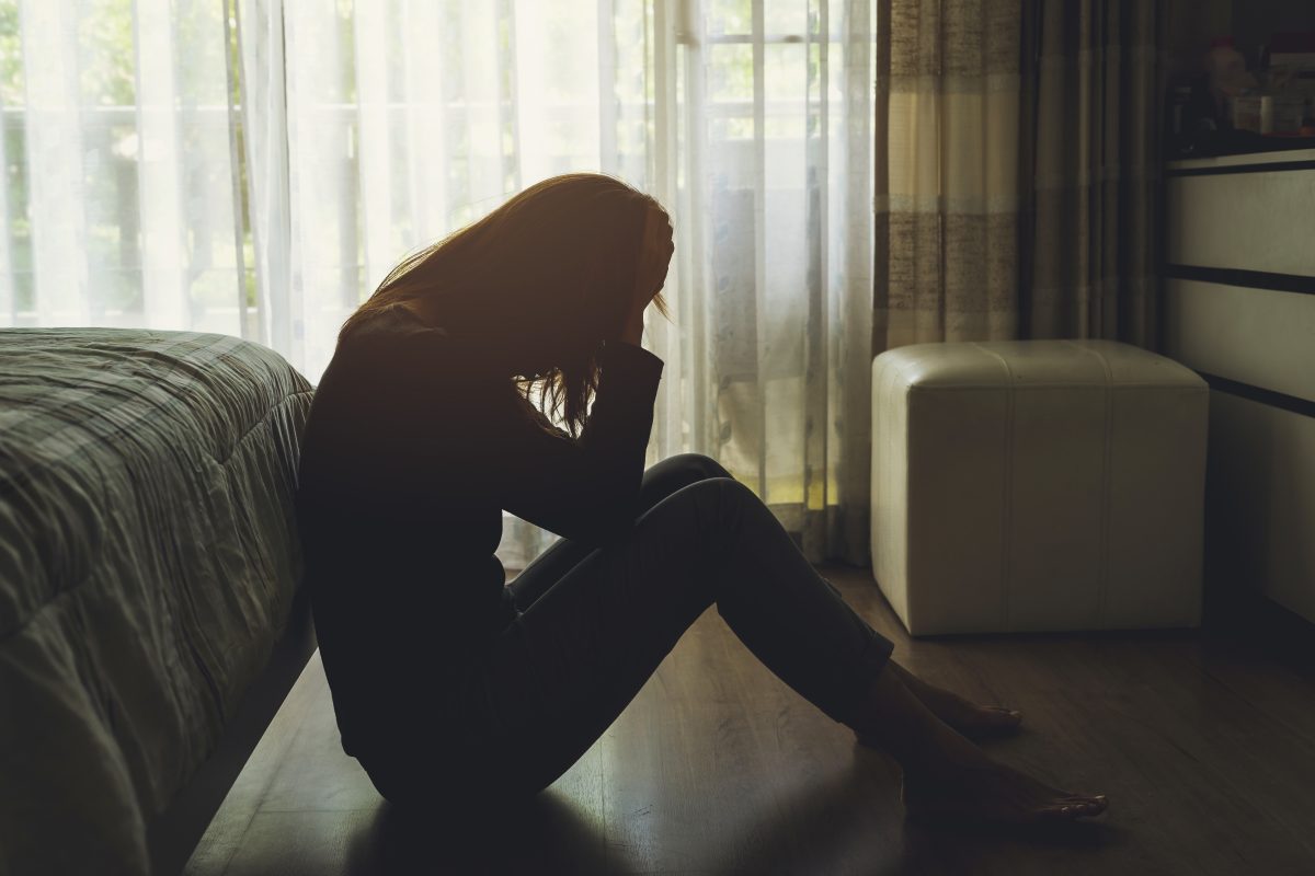 Silhouette of a domestic violence victim slumped onto a bedroom floor with her head in her hands