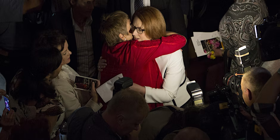 Julia Gillard embracing a person surrounded by television cameras.