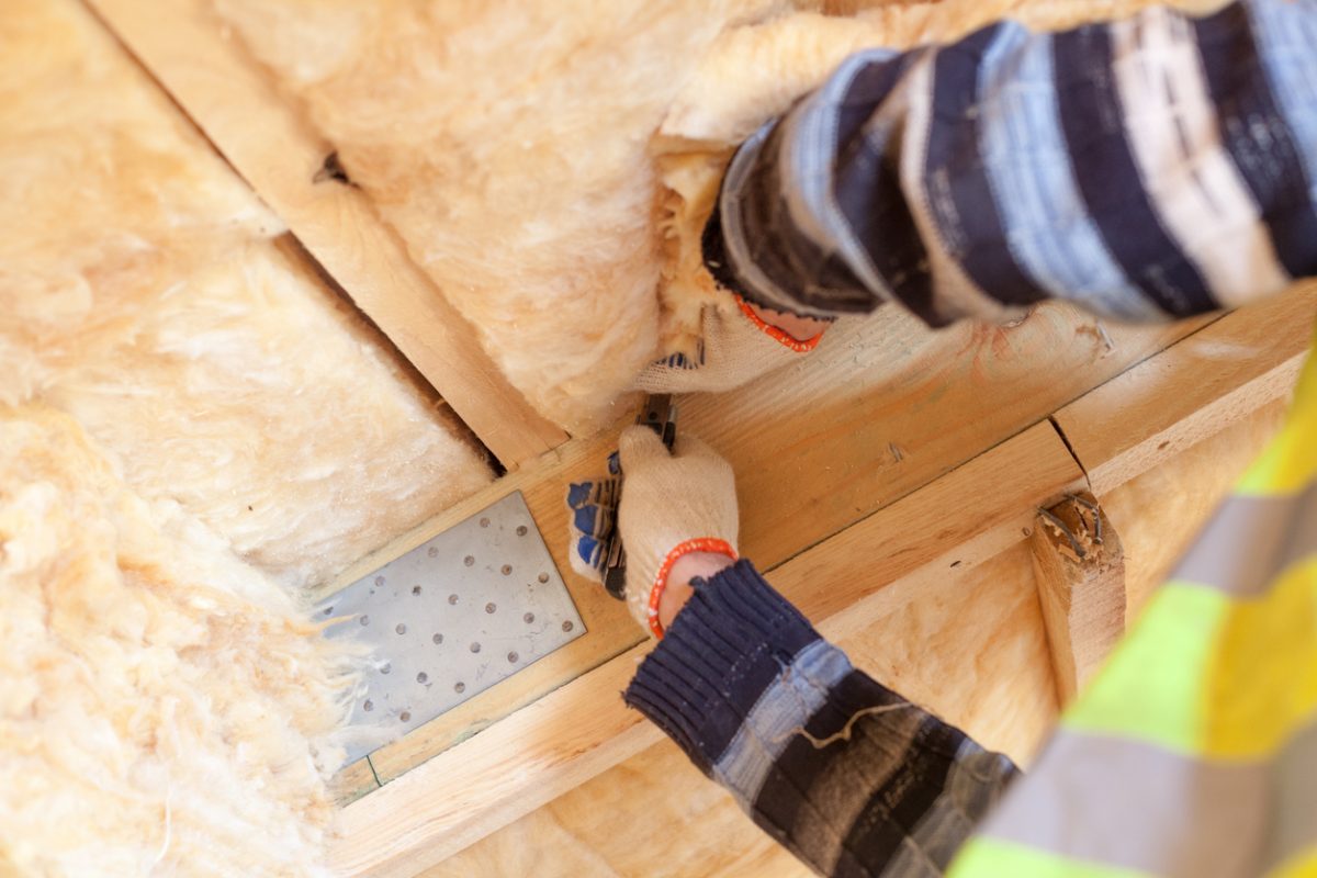 Cropped view of professional workman holding knife tool in hands and cutting rockwool insulation material on ceiling in new house
