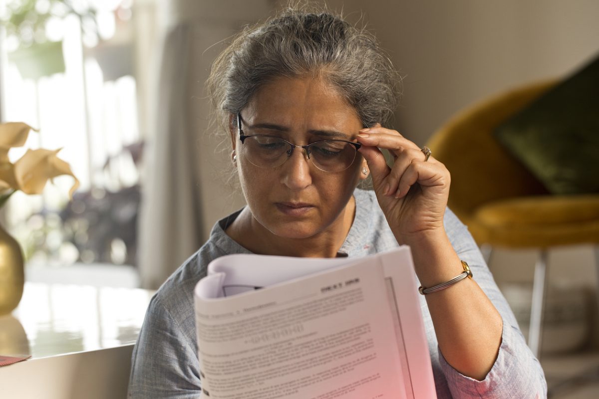 Asian woman peers through her spectacles at a piece of paper and looks worried