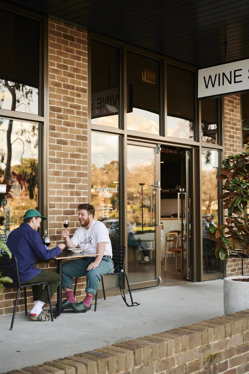 Two men in crocs drink wine out the front of the Paranormal wines shopfront