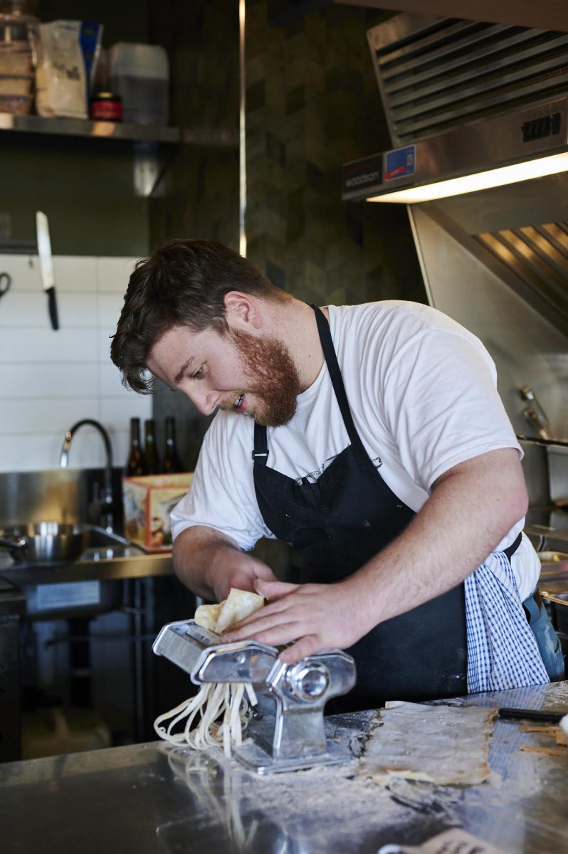 Chef in white tshirt and black apron rolls pasta through a machine