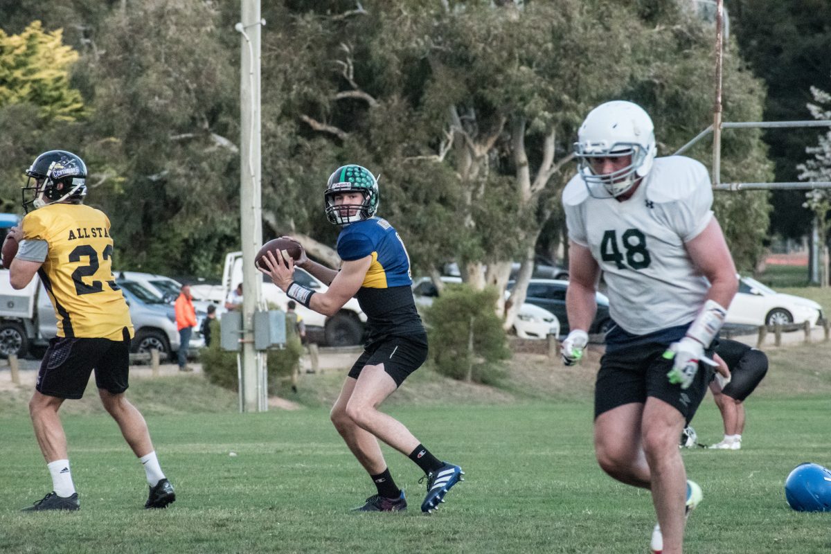 Hennecke, Lyle and Griffiths on a green football field in training gear with a line of parked cars behind. 