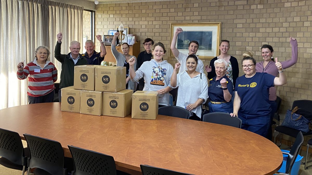 Birthing Kit Packing Event featuring people crowded around a table with packed boxes of birthing kits.