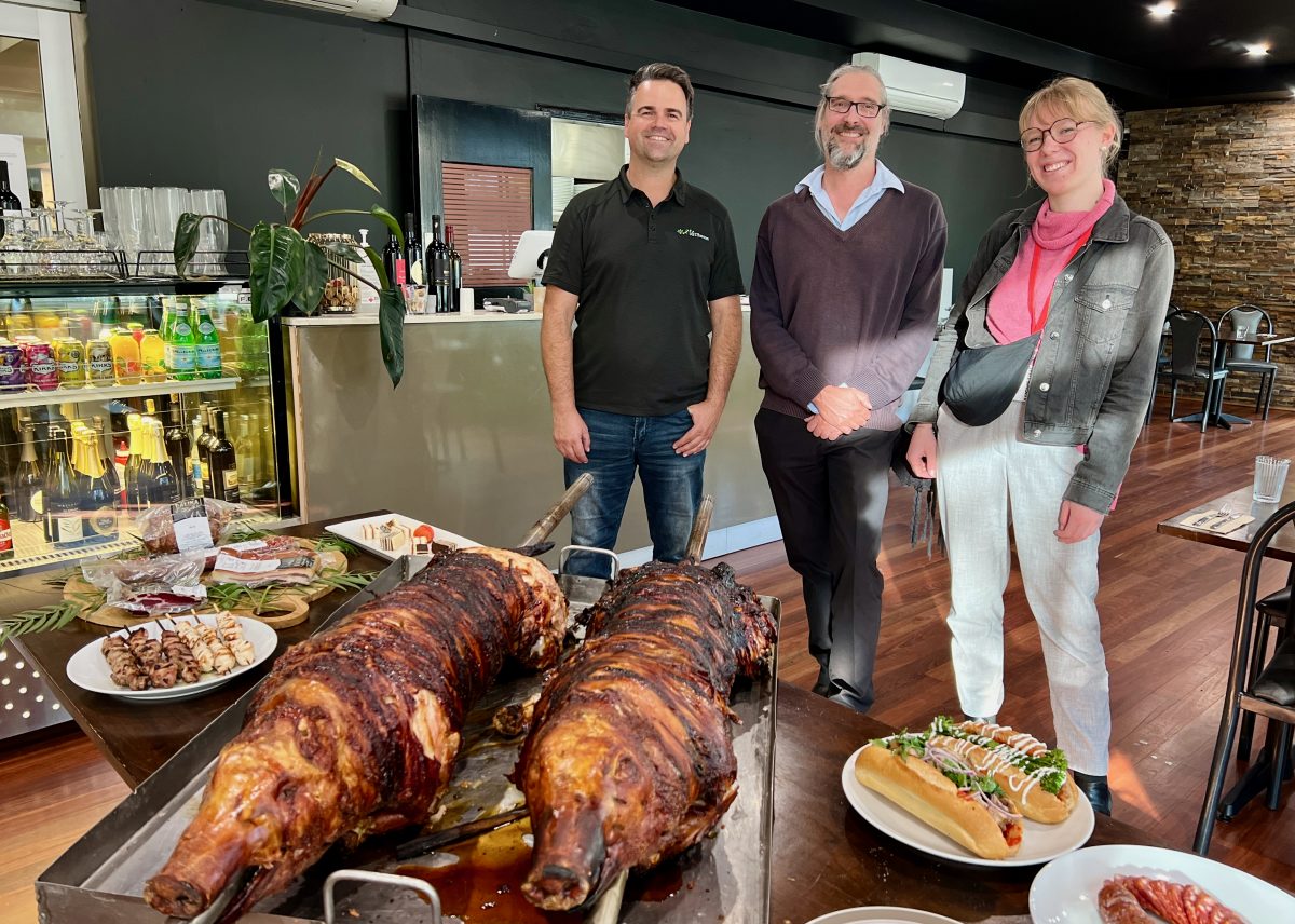 Three people smile behind a table laden with food.