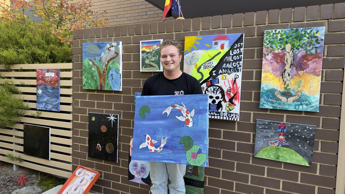 Nick Barker holding his artwork in front of a wall of other artworks.