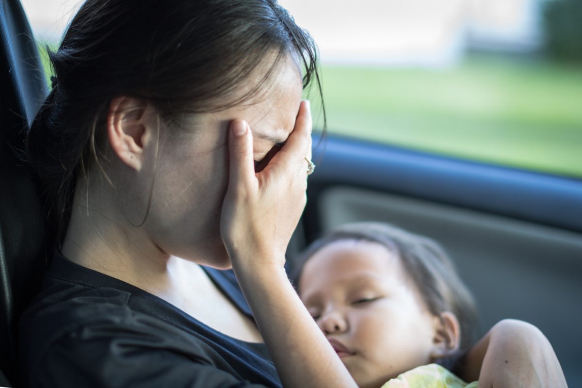 Woman sits stressed out in her car, holding a sleeping toddler