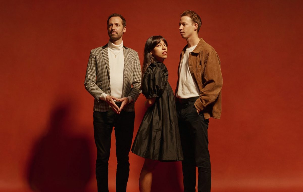 two man and a woman standing in front of a red screen