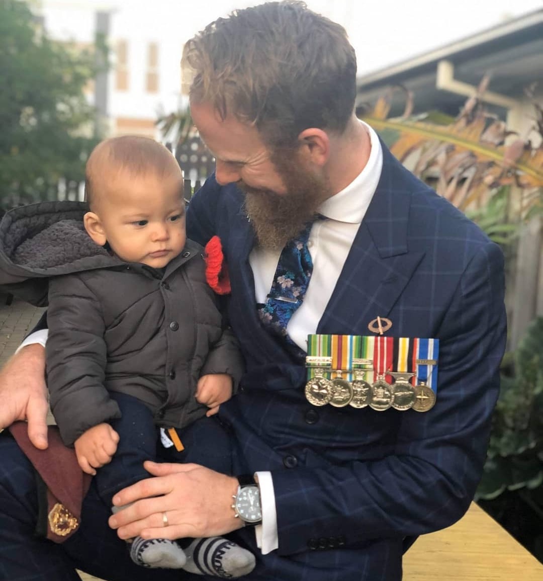 Man in suit wearing army medals holds his baby