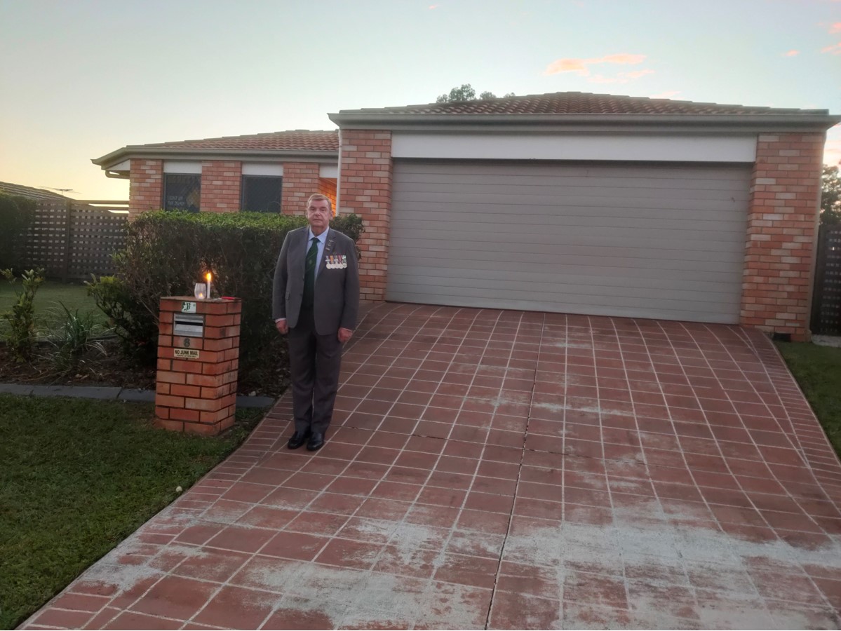 Man stands in a suit outside the front of a home with military medals pinned to his jacket and a candle lit on the mailbox