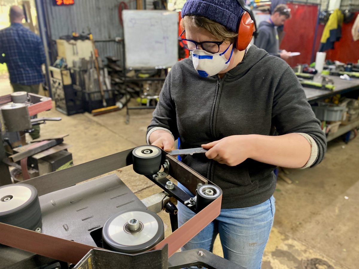 Lucy wearing safety gear working with a knife on a grinder