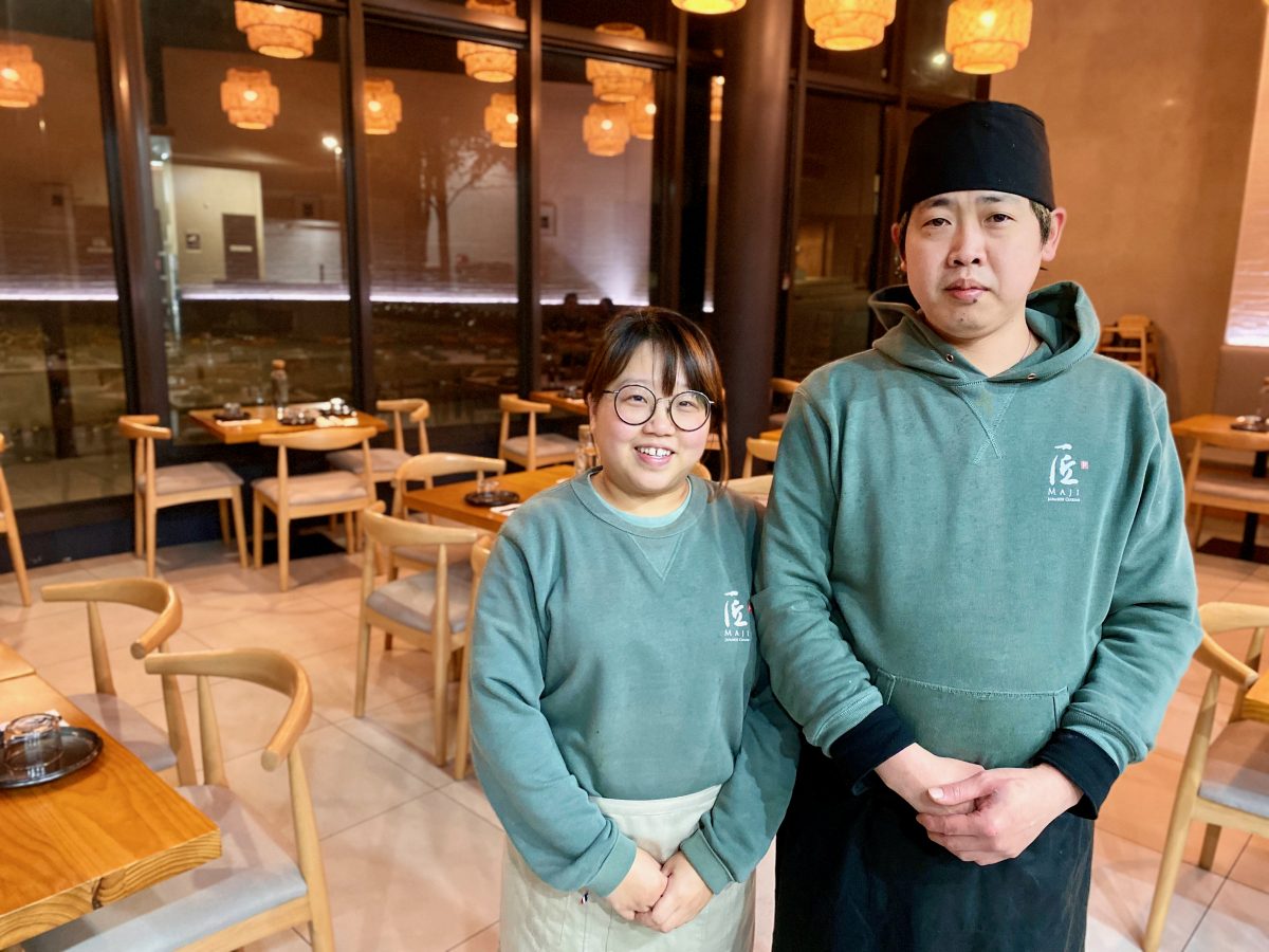 Woman and man in green Maji branded jumpers stand in restaurant