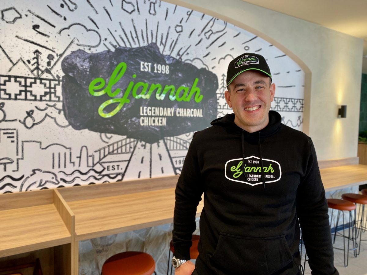 Christian wears El Jannah branded jumper and hat in front of sign in shop