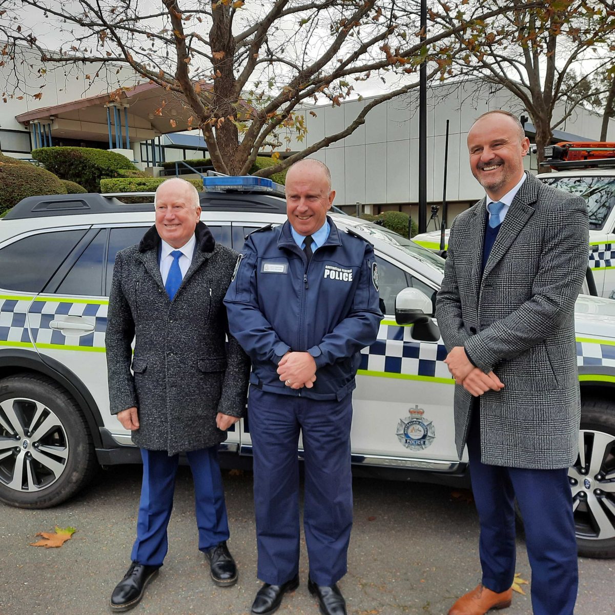 three men in front of police vehicle