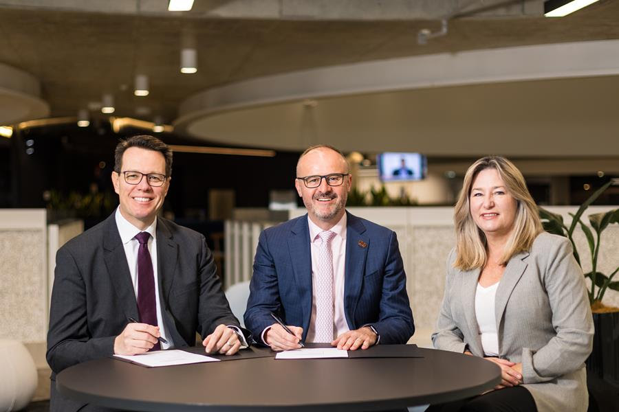 two men and a woman sitting at a table signing papers