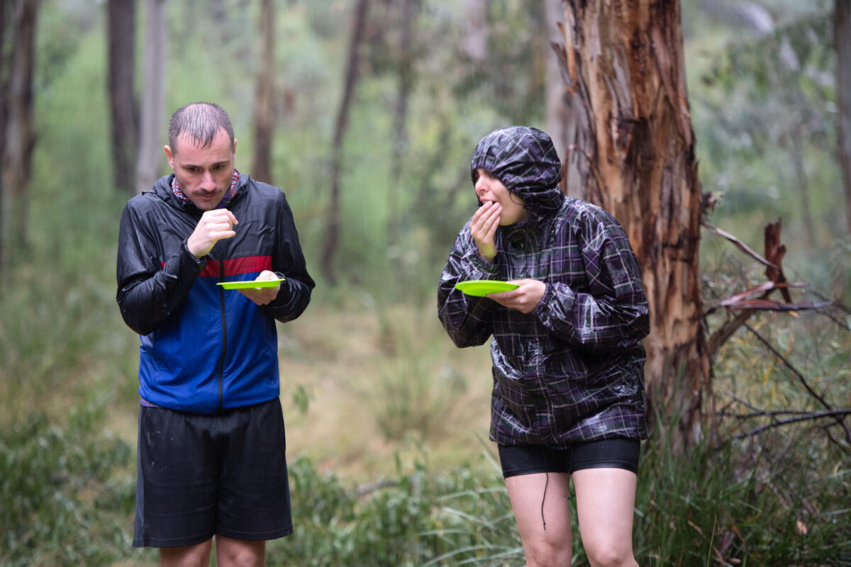 Two contestants holding plates eating outdoors