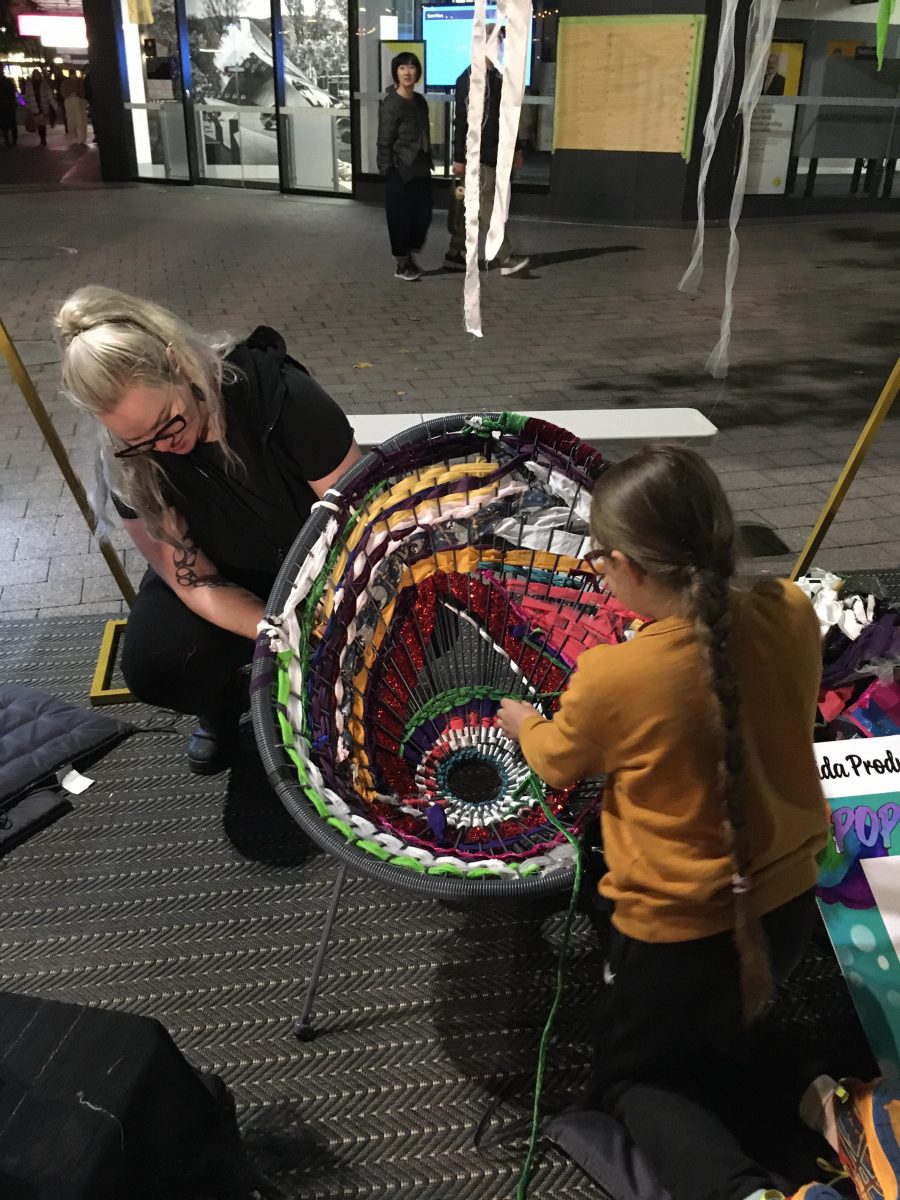 A mother and her child weave ribbons through a chair in Garema Place.