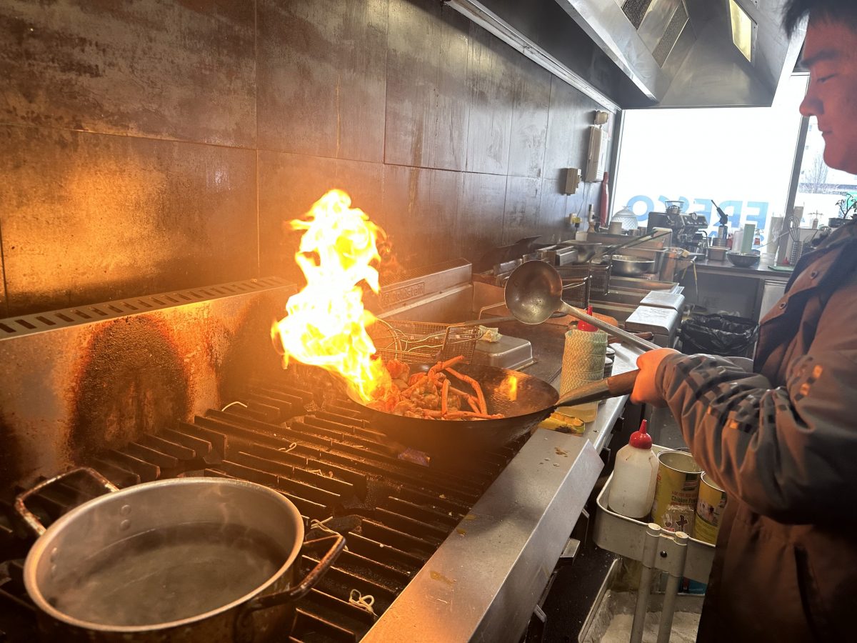A chef cooks lobster in a wok with a flame rising above it.