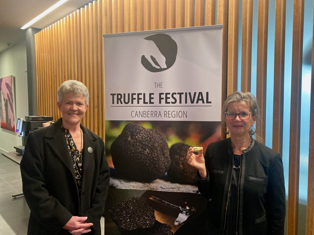 Two women pose next to truffle festival signage