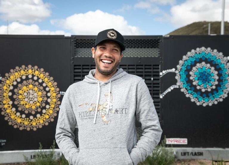 man smiling next to mural on electrical substation