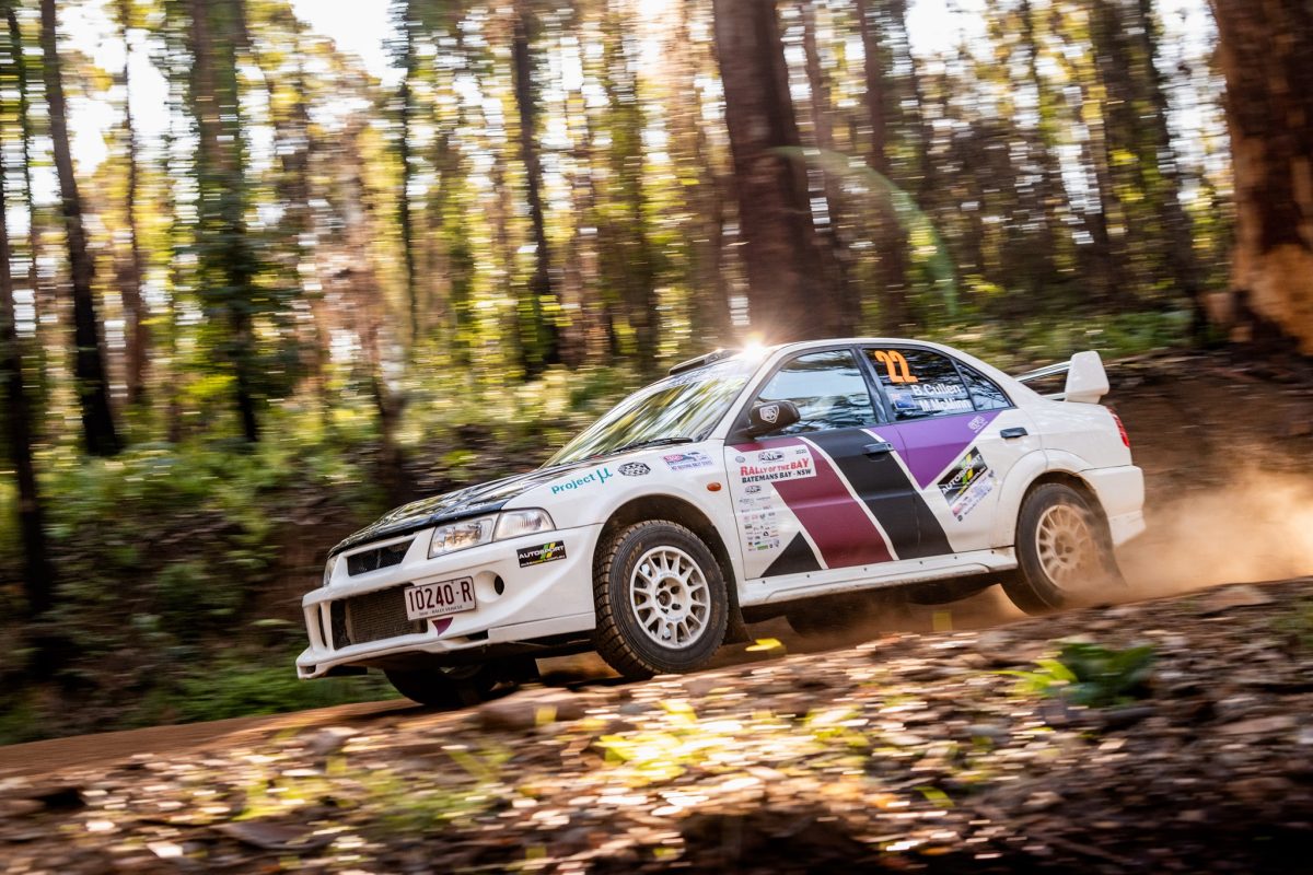 A rally car driving past on a track in the middle of the bush.