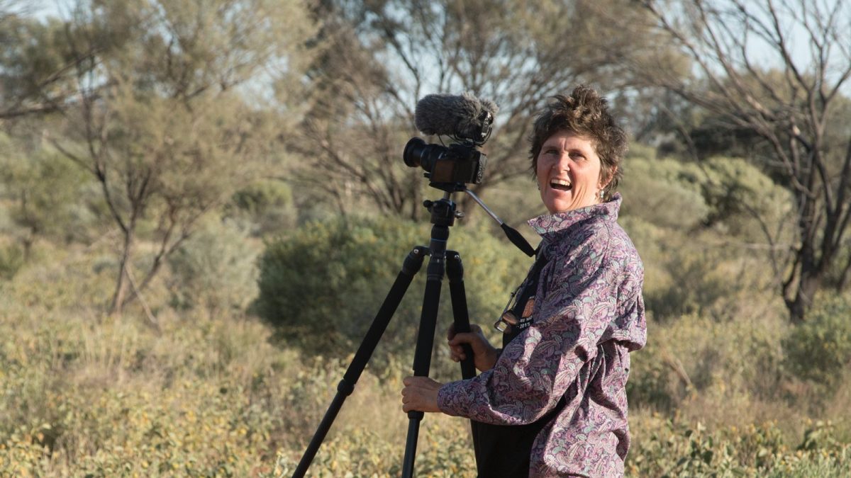 Ethnoecologist Fiona Walsh smiles as she stands behind a camera in the Australian outback