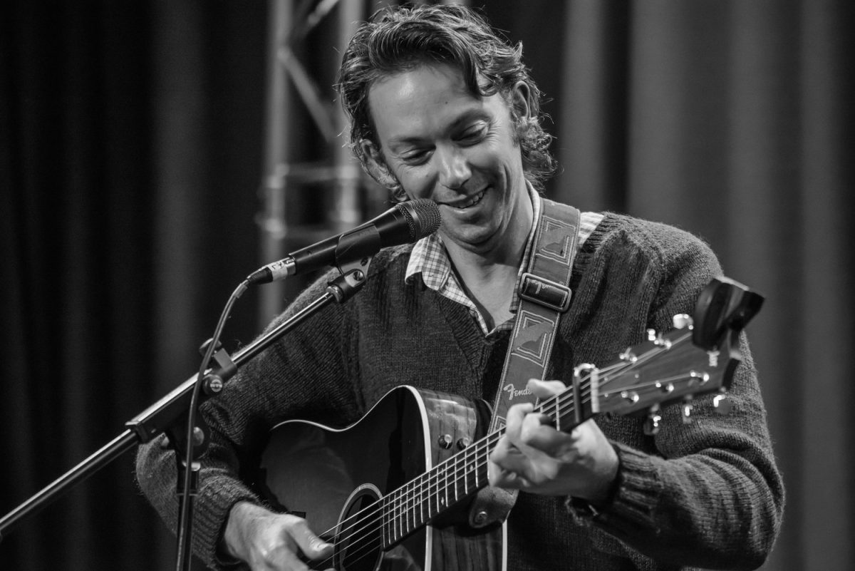 Black and white photo of Dan Challis singing into a microphone and playing guitar