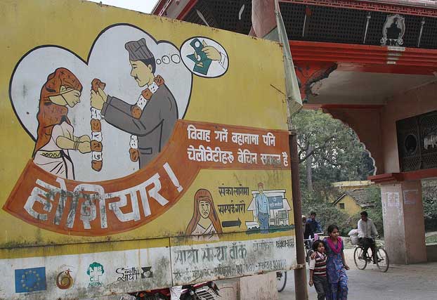 A sign in Nepal next to a road with children and people on bikes on it.