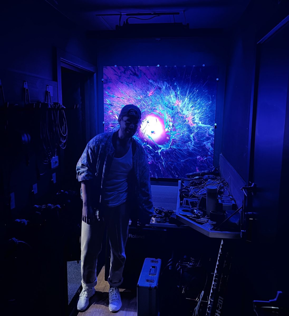 Daniel Keo standing in front of a psychedelic painting in his studio.