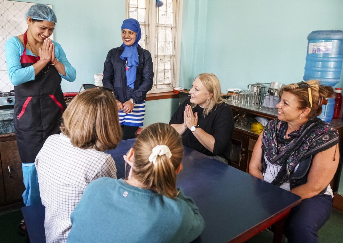 A Nepali woman says hello to the travelling group sitting around a kitchen table.