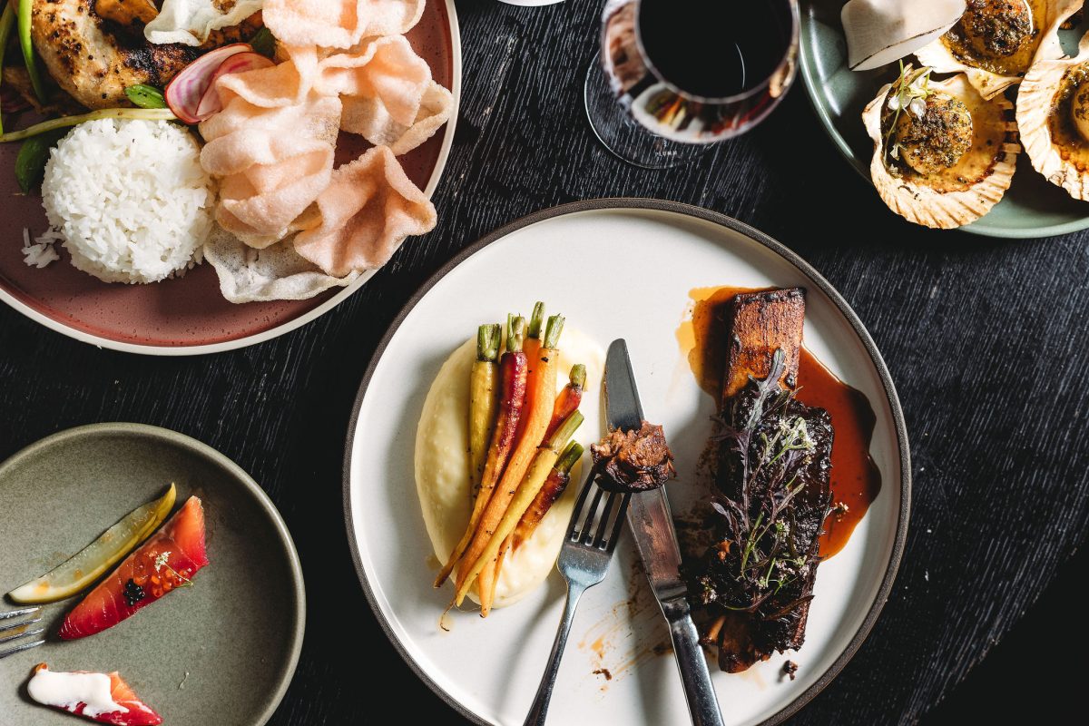 Multiple dishes on a table with a full wine glass in the centre.