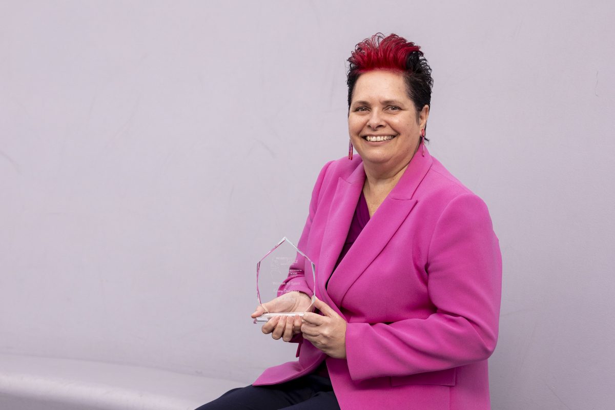 Dr Karen Demmery holds an award and smiles