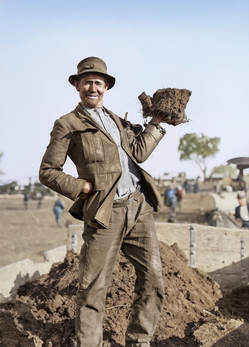 Old photo of a man holding a sod of dirt at Parliament House.